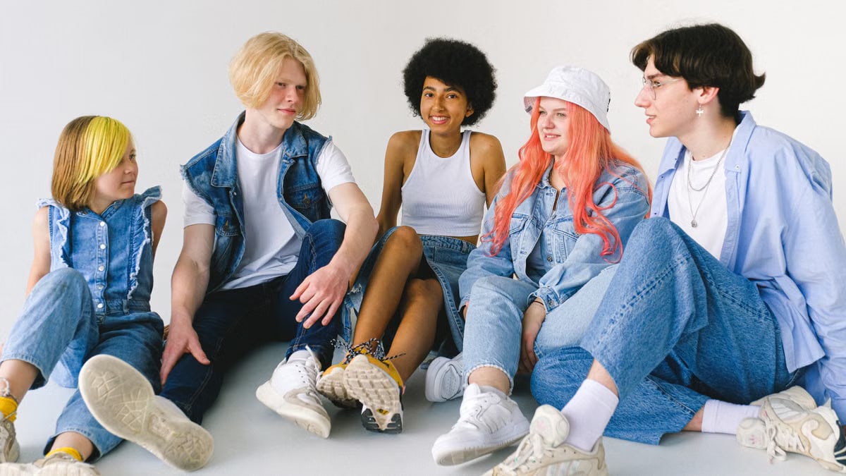 Group of cheerful diverse teenager friends talking to each other while sitting together on floor against white background